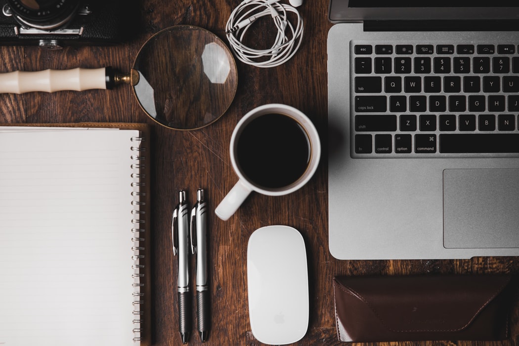 A picture of a desk with a computer, notebook and coffee on it